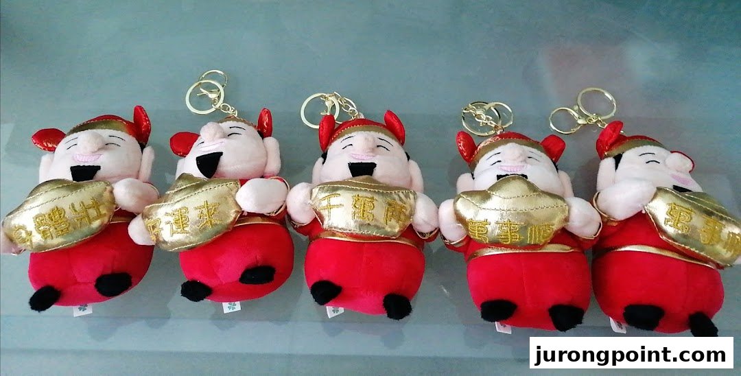 Five plush keychains depicting smiling figures in red holding golden ingots, likely claw machine prizes.