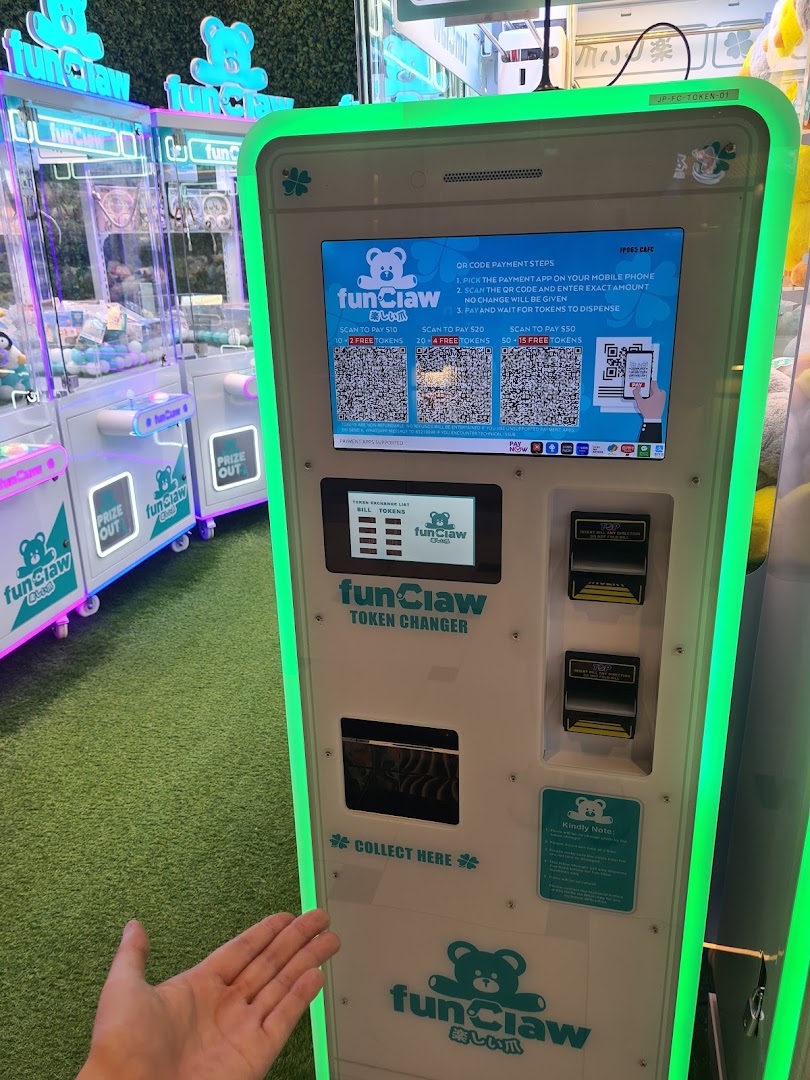 A Fun Claw token changer machine with QR code payment options and claw machines in the background.