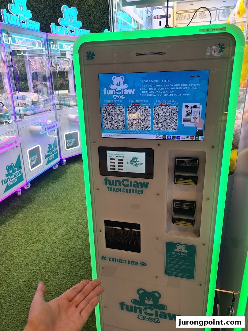 A Fun Claw token changer machine with QR code payment options and claw machines in the background.