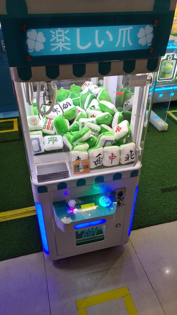 A brightly lit claw machine filled with green and white mahjong tile plush toys.