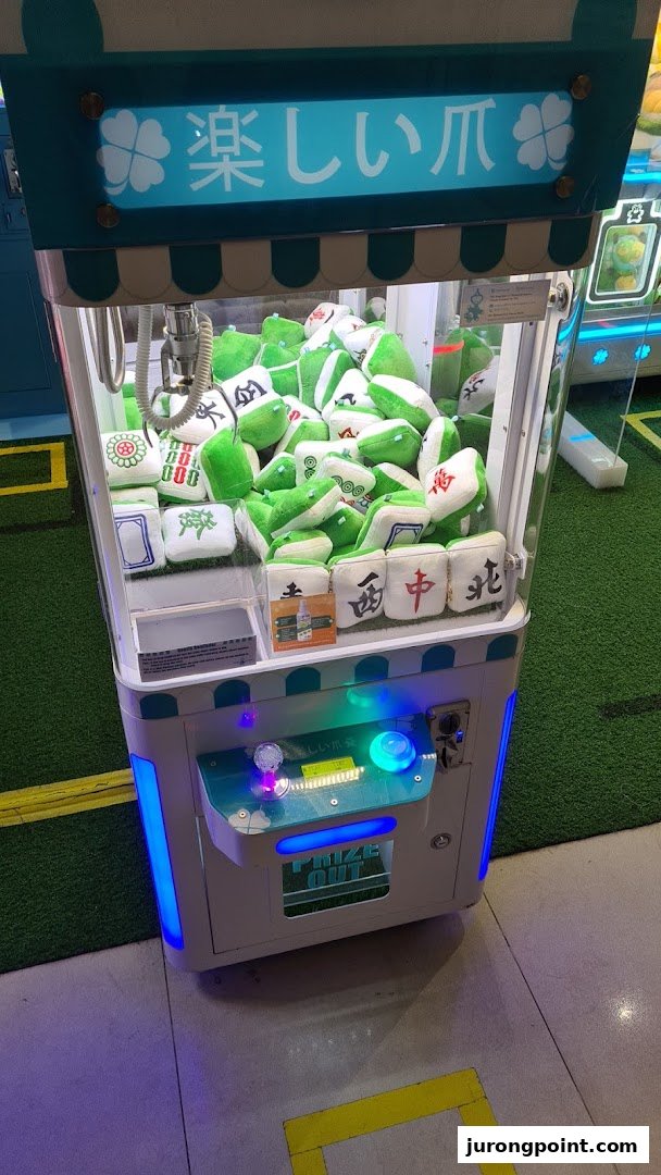 A brightly lit claw machine filled with green and white mahjong tile plush toys.