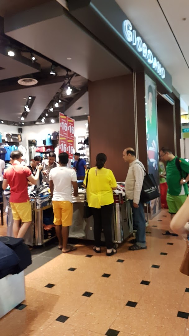 Customers browse clothing items at the entrance of a Giordano retail store, featuring visible sale signs.