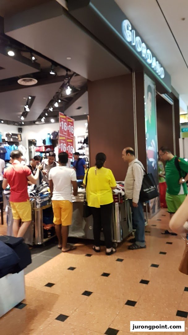 Customers browse clothing items at the entrance of a Giordano retail store, featuring visible sale signs.