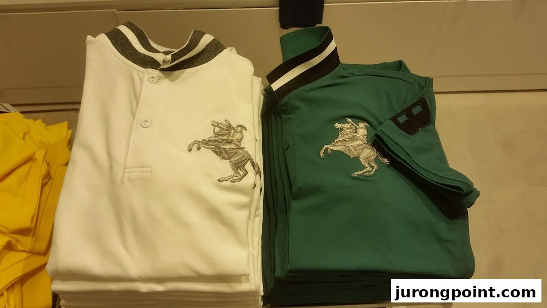 Two folded polo shirts, white and green, with a horse rider emblem, displayed in a retail store.