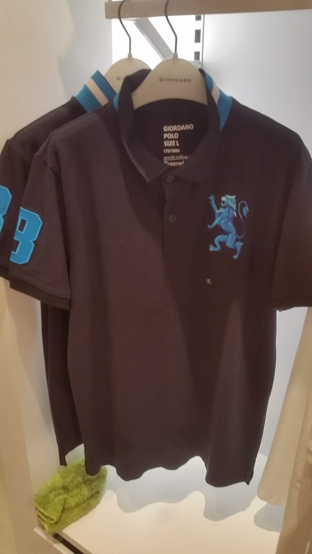 A dark Giordano polo shirt with a blue lion logo and striped collar hangs in a retail store.
