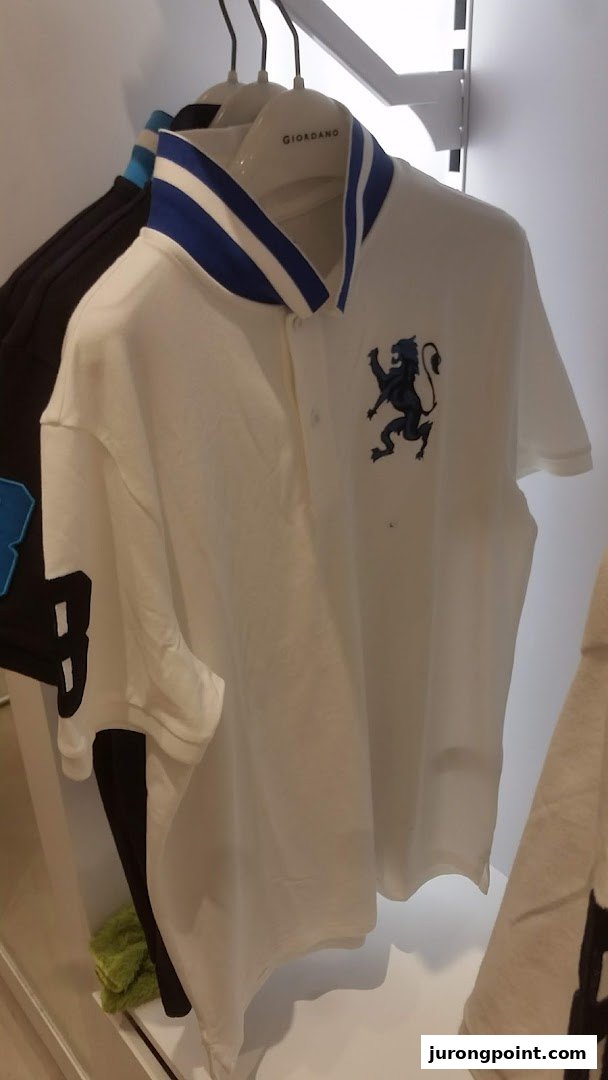 A white polo shirt with a blue-striped collar and a black lion emblem hangs in a Giordano store.