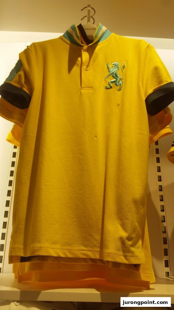 A vibrant yellow polo shirt with a green lion emblem and striped collar hangs in a retail store.