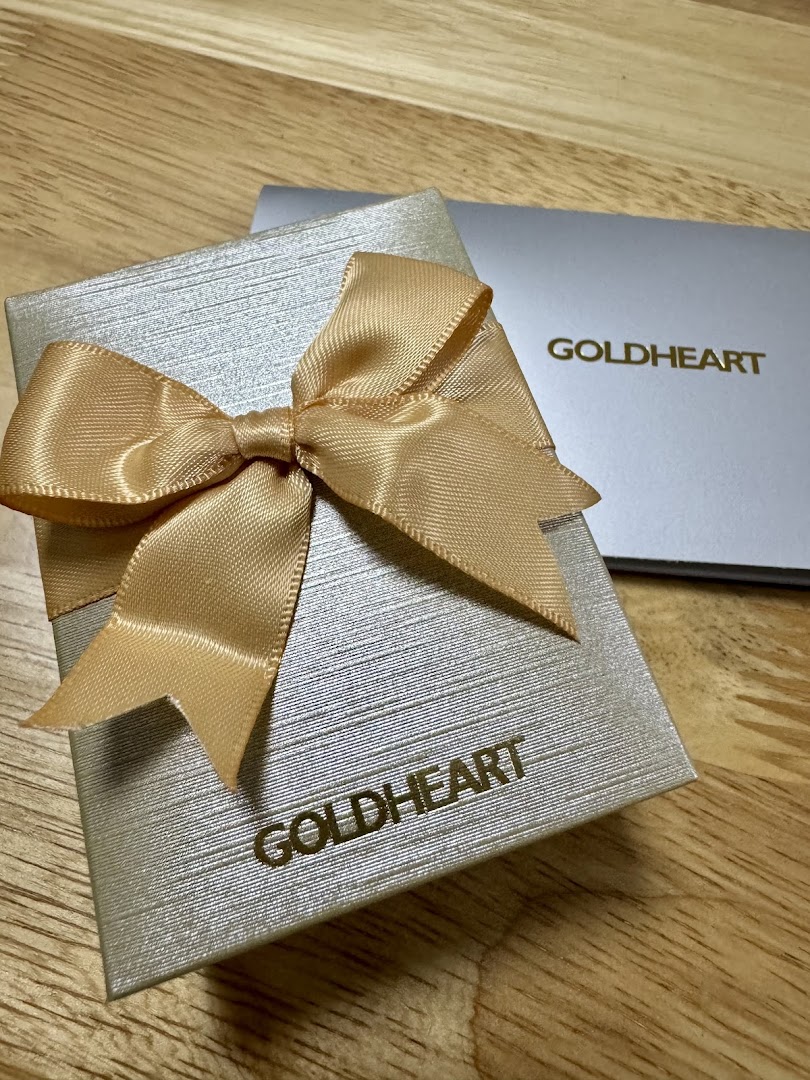 A silver Goldheart jewelry gift box with a gold ribbon bow on a wooden surface.