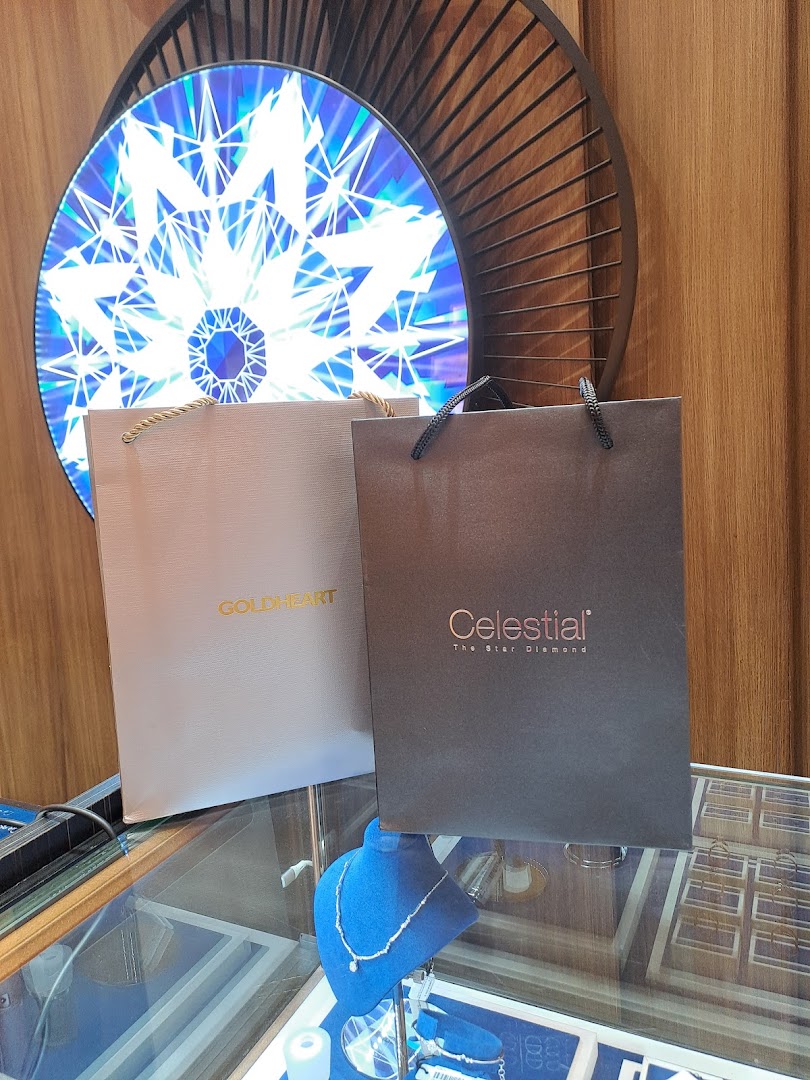 Two Goldheart and Celestial shopping bags on a display case with jewelry, illuminated by a decorative light.