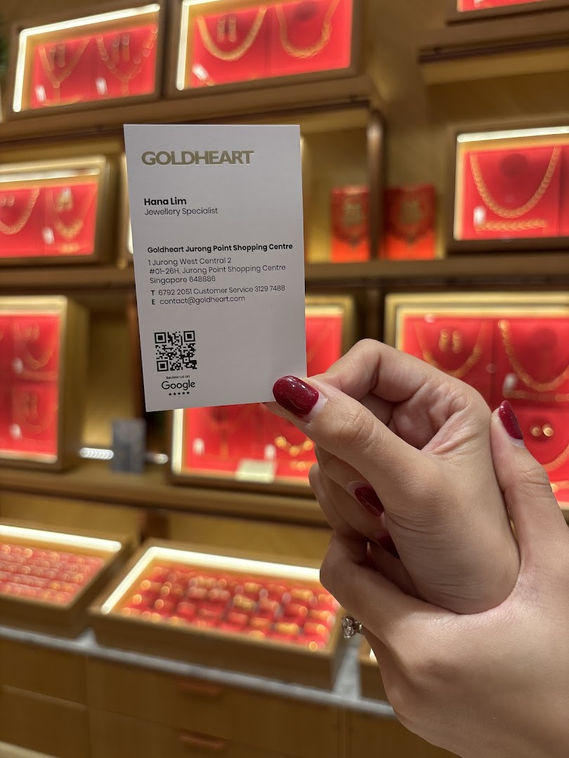 A hand holds a Goldheart business card in front of illuminated jewelry display cases.