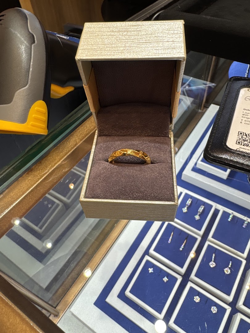 A gold ring displayed in an open box on a glass counter with other jewelry.