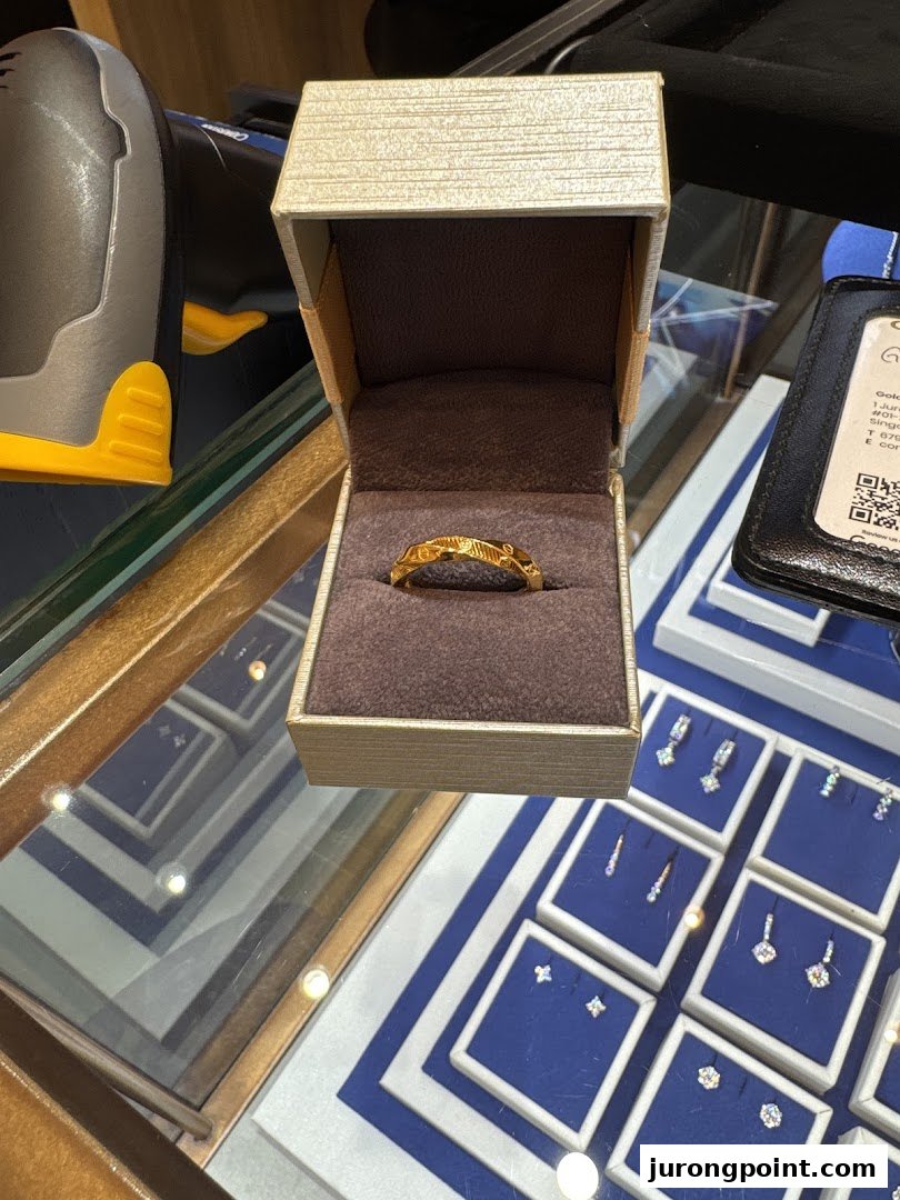 A gold ring displayed in an open box on a glass counter with other jewelry.