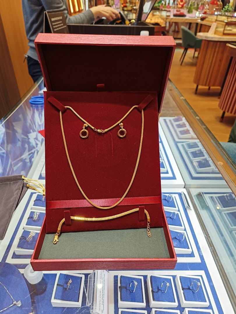 A gold necklace, bracelet, and earrings set displayed in a red box on a jewelry counter.