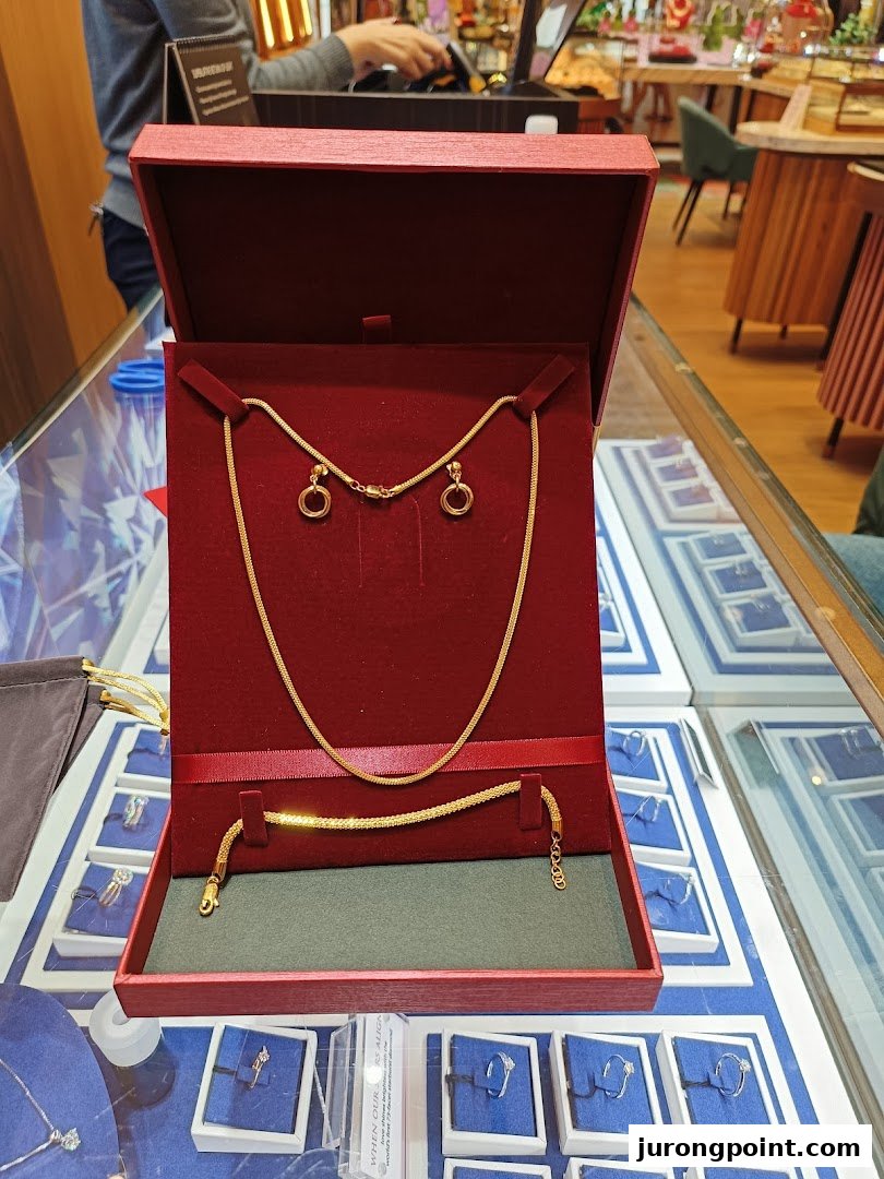 A gold necklace, bracelet, and earrings set displayed in a red box on a jewelry counter.