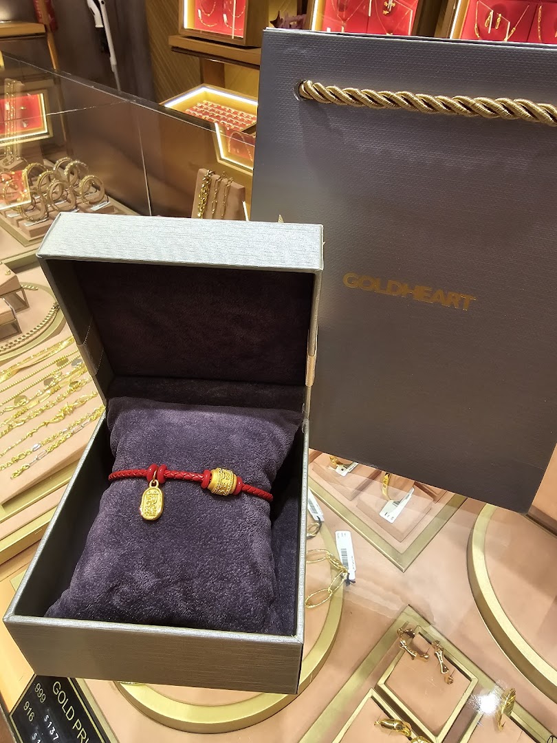 A red bracelet with gold charms displayed in an open jewelry box, with a Goldheart shopping bag.