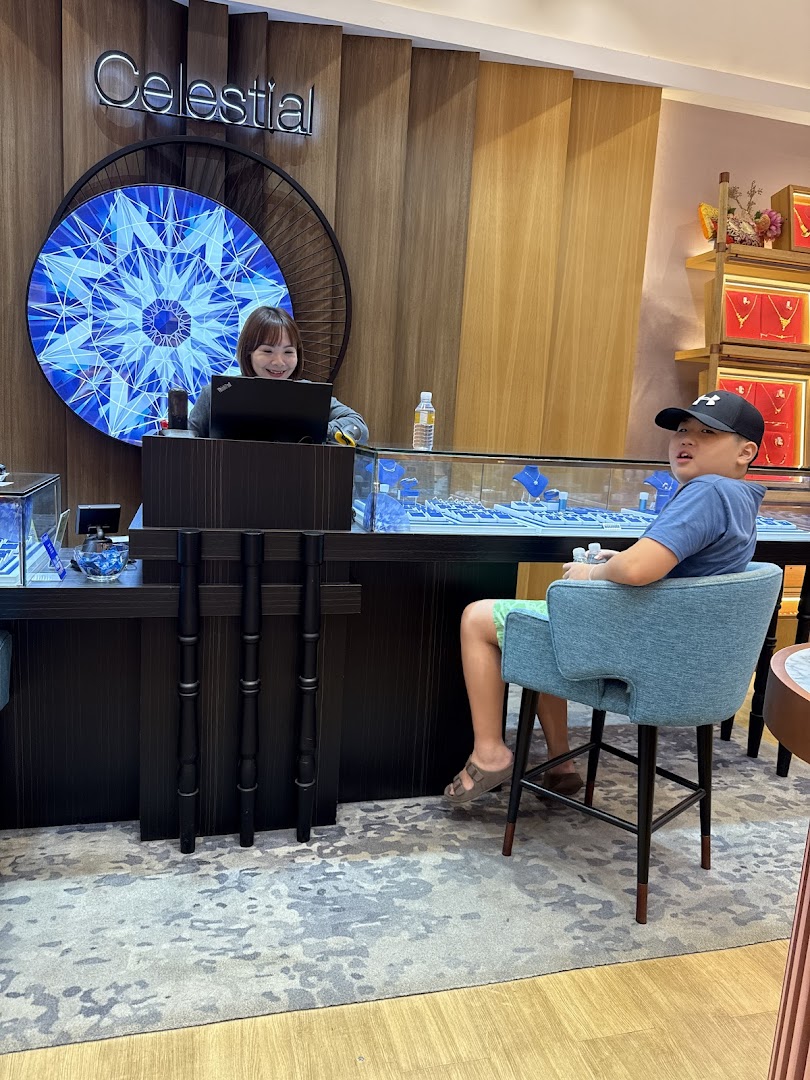 A Goldheart Jewelry staff member smiles behind a counter with jewelry displays, while a young customer sits nearby.