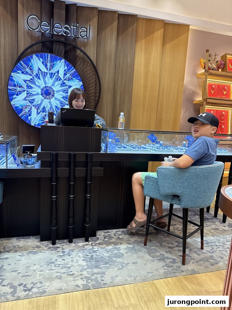 A Goldheart Jewelry staff member smiles behind a counter with jewelry displays, while a young customer sits nearby.