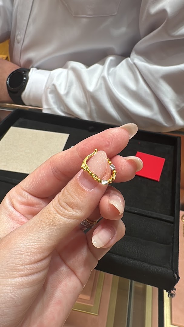 A hand holds a unique gold and silver jewelry piece, possibly an earring or charm, inside Goldheart Jewelry.