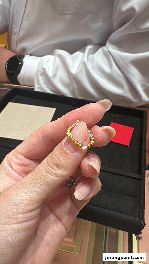 A hand holds a unique gold and silver jewelry piece, possibly an earring or charm, inside Goldheart Jewelry.