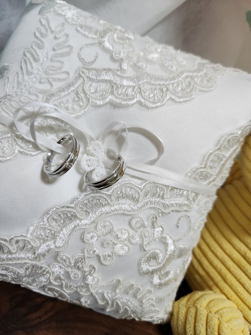 Two elegant silver rings with subtle details resting on a white, lace-embroidered ring pillow.