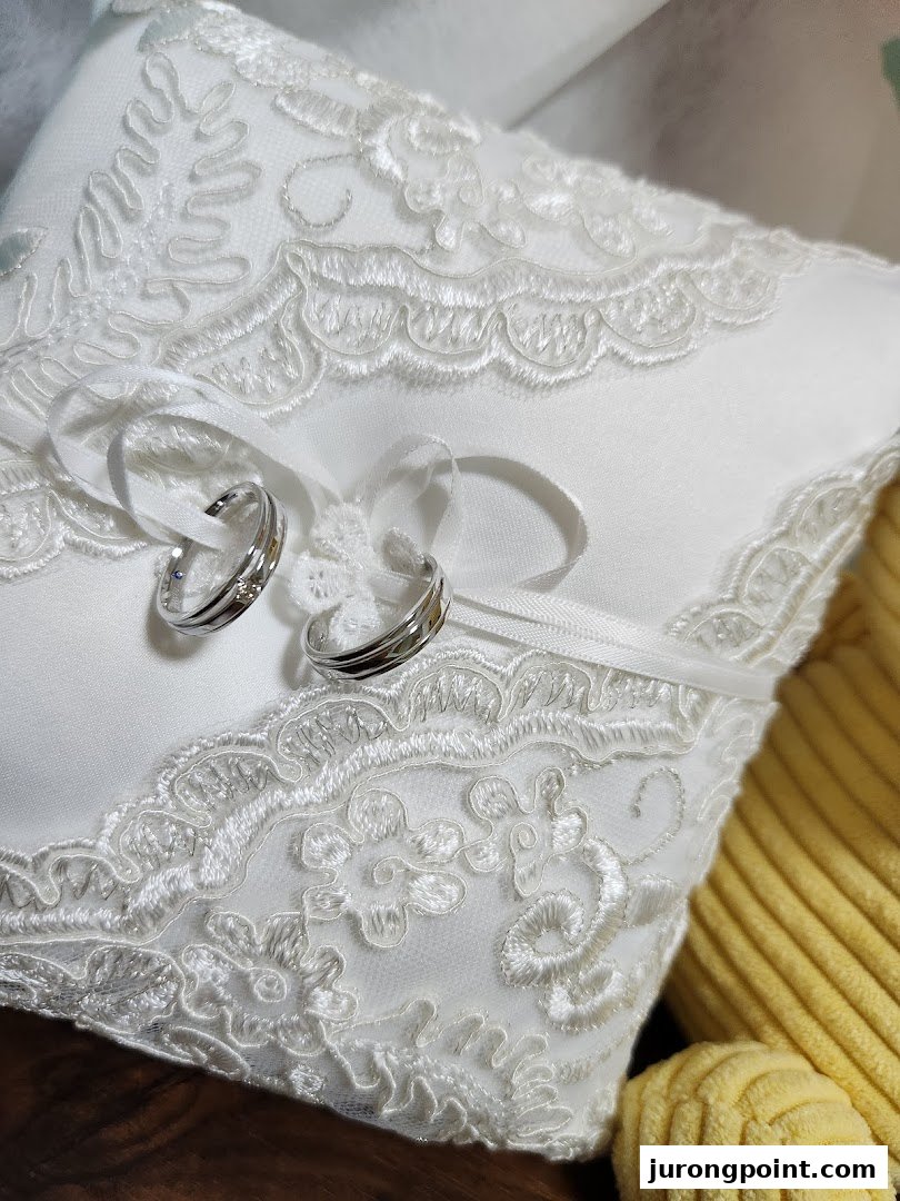 Two elegant silver rings with subtle details resting on a white, lace-embroidered ring pillow.