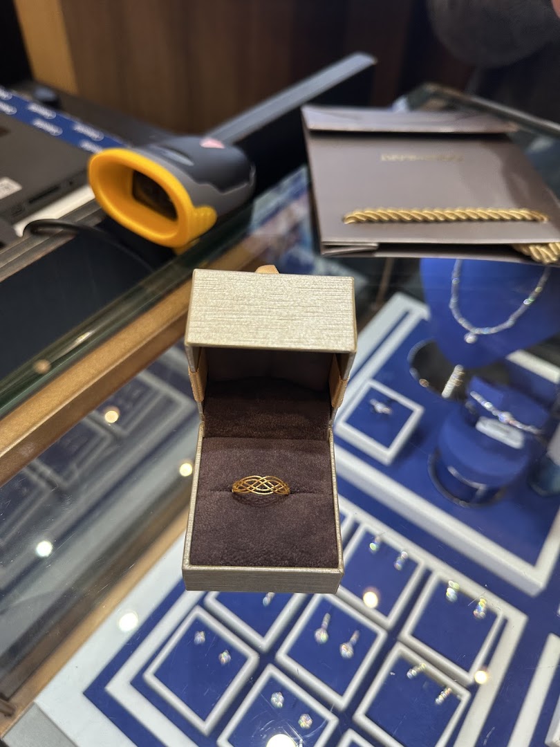 A gold ring in an open box on a display counter, surrounded by other jewelry items.