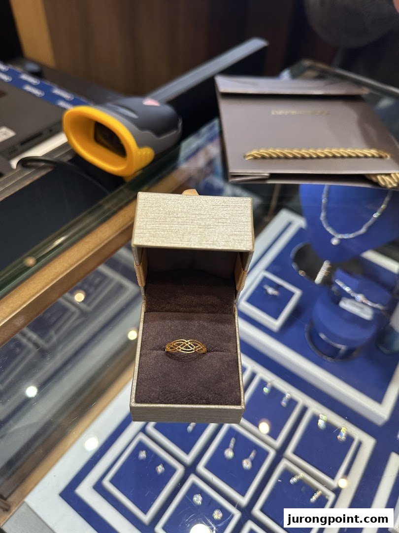 A gold ring in an open box on a display counter, surrounded by other jewelry items.