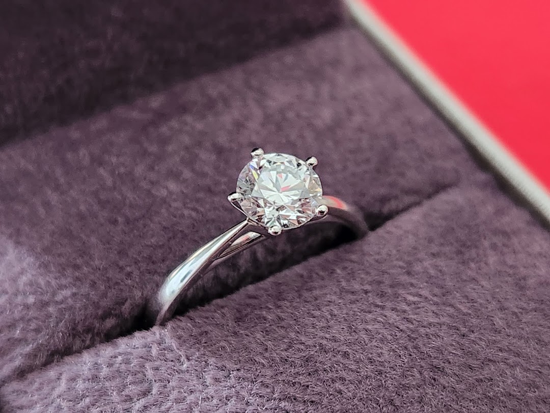 A close-up of a sparkling diamond solitaire ring set in a silver band, resting in a purple velvet box.