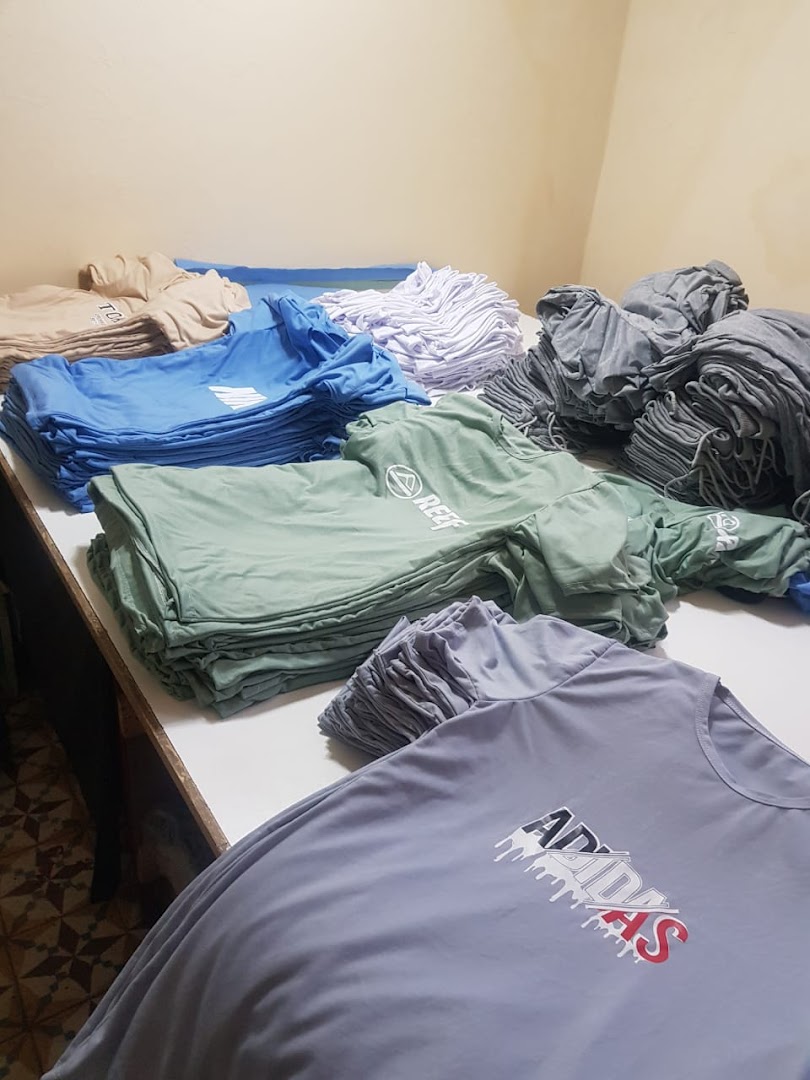 Stacks of various colored t-shirts with different brand logos on a table.