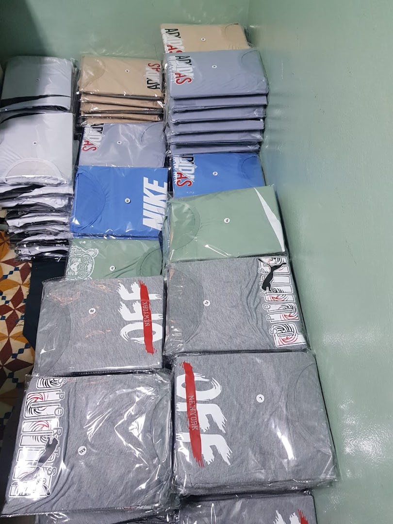 Neatly stacked, packaged t-shirts featuring various brand logos in a retail setting.