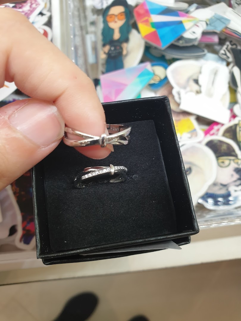 A hand holds a silver ring, with another ring displayed in a black box, amidst various small accessories.