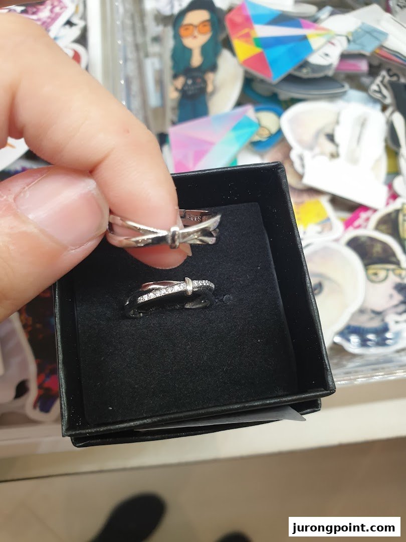 A hand holds a silver ring, with another ring displayed in a black box, amidst various small accessories.
