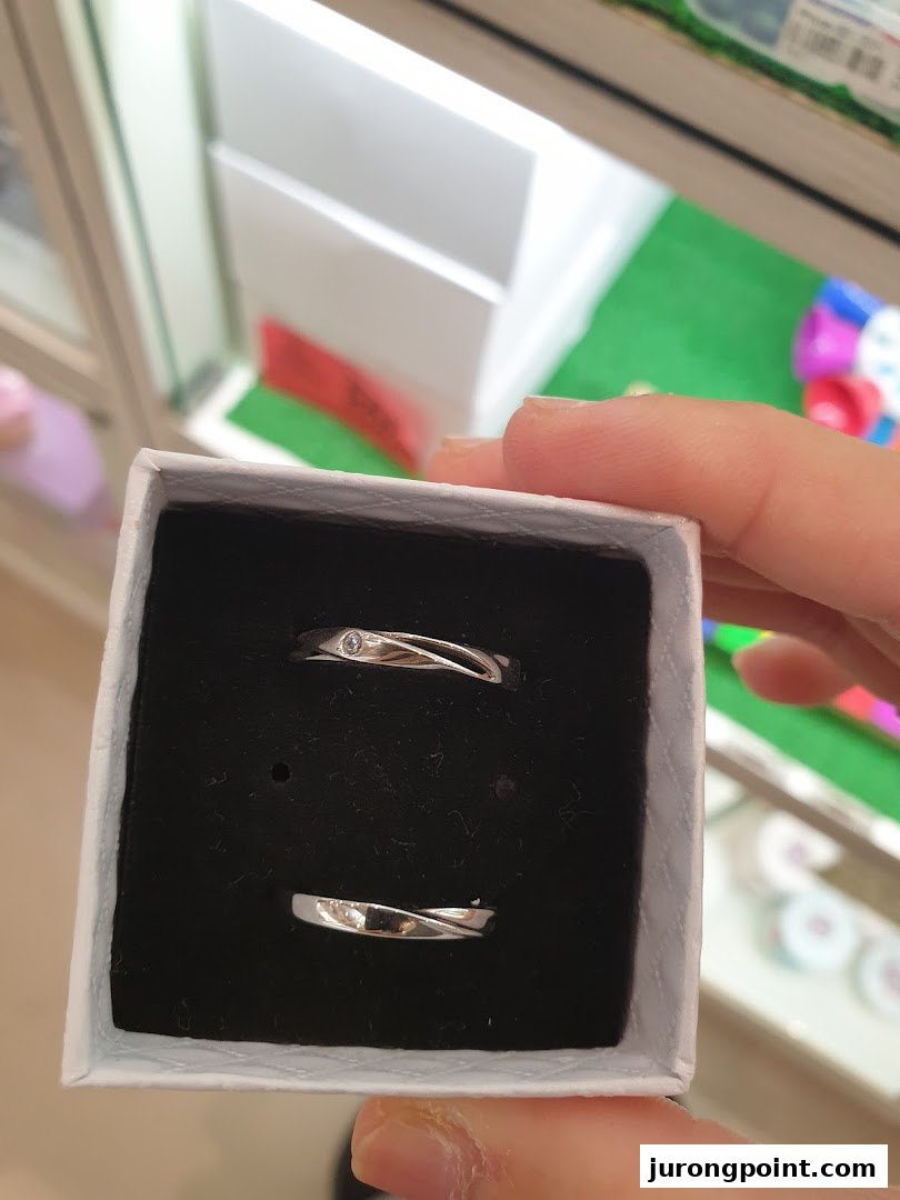 A hand holds a small box displaying a pair of elegant silver rings with subtle designs.