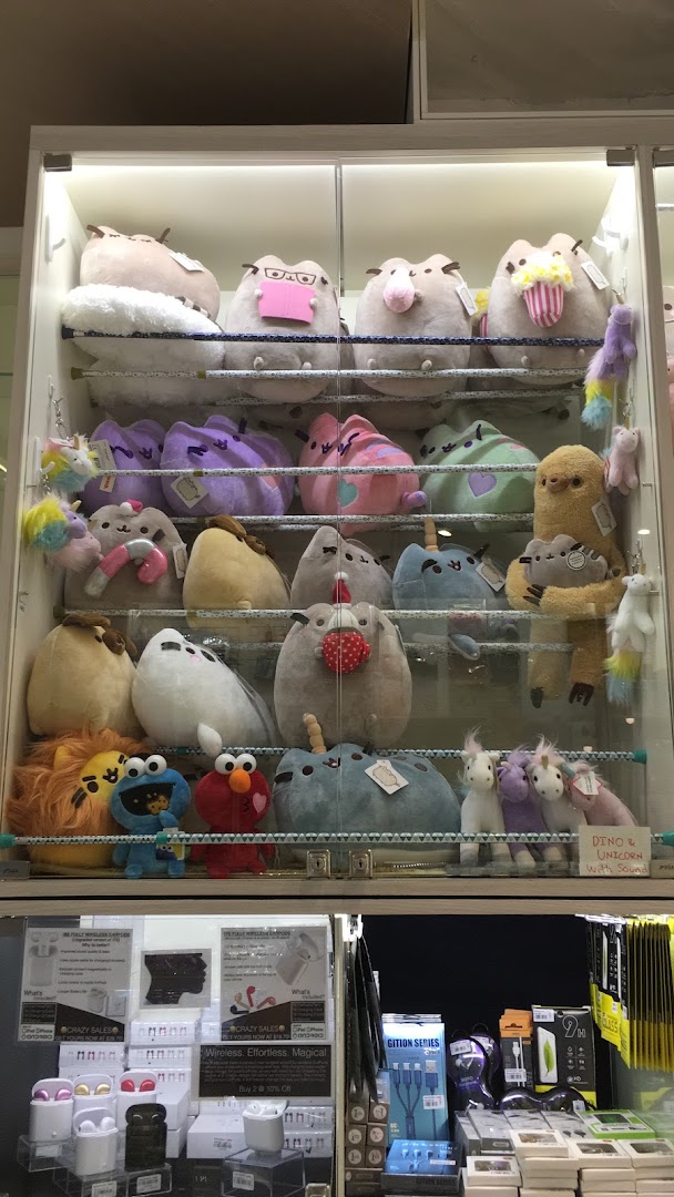 A display cabinet at Hako featuring a wide variety of plush toys, including Pusheen, and a lower section with electronics.