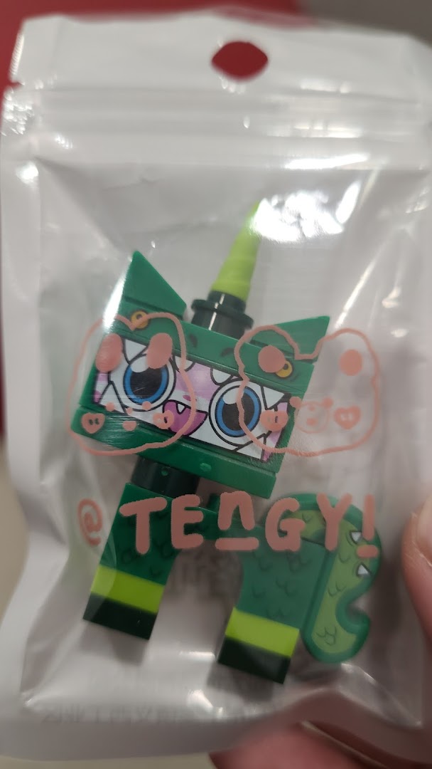 A green building block figure resembling a dragon-unicorn hybrid, packaged in clear plastic with pink graphics.
