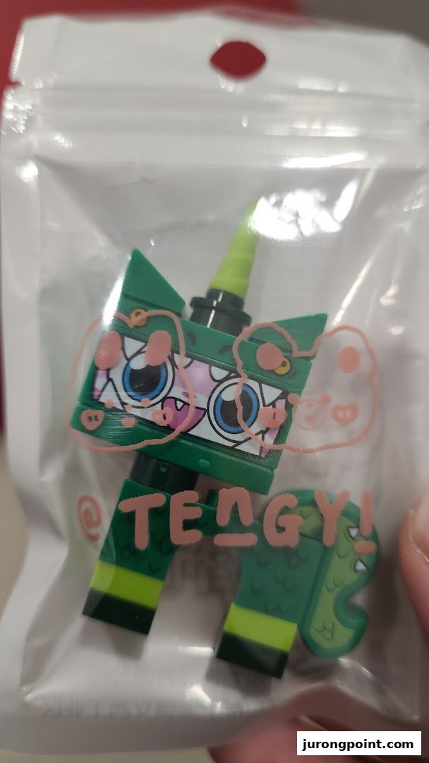 A green building block figure resembling a dragon-unicorn hybrid, packaged in clear plastic with pink graphics.