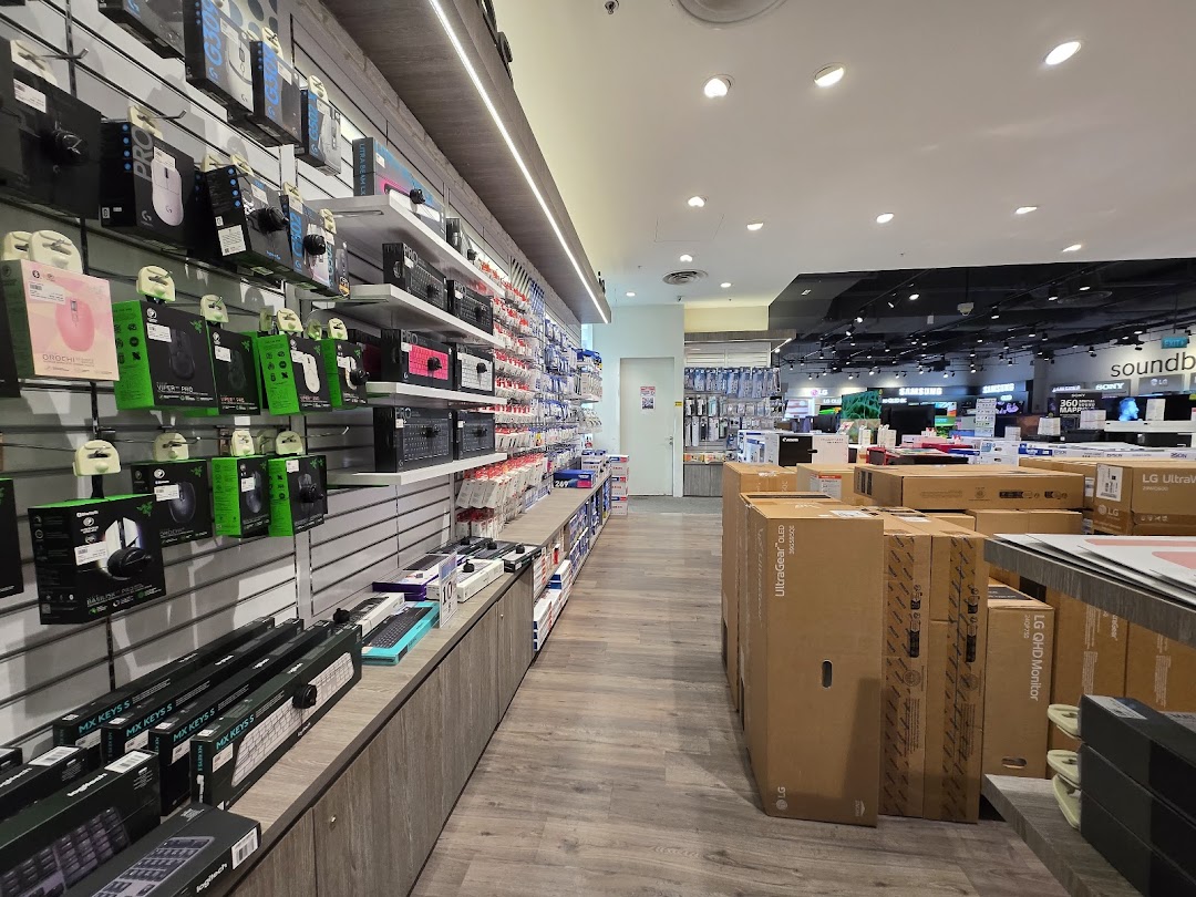 An aisle in an electronics store showcasing computer peripherals, gaming gear, and boxed monitors.