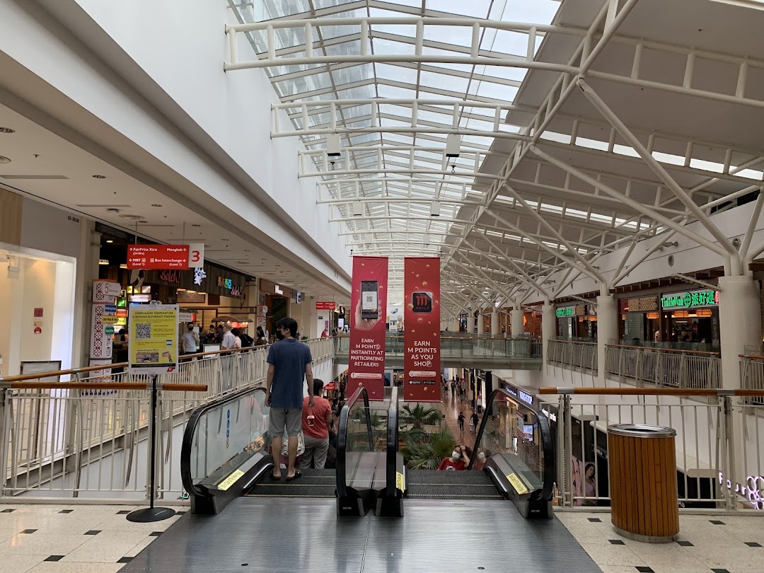 View of a bustling shopping mall interior with escalators and various retail outlets.
