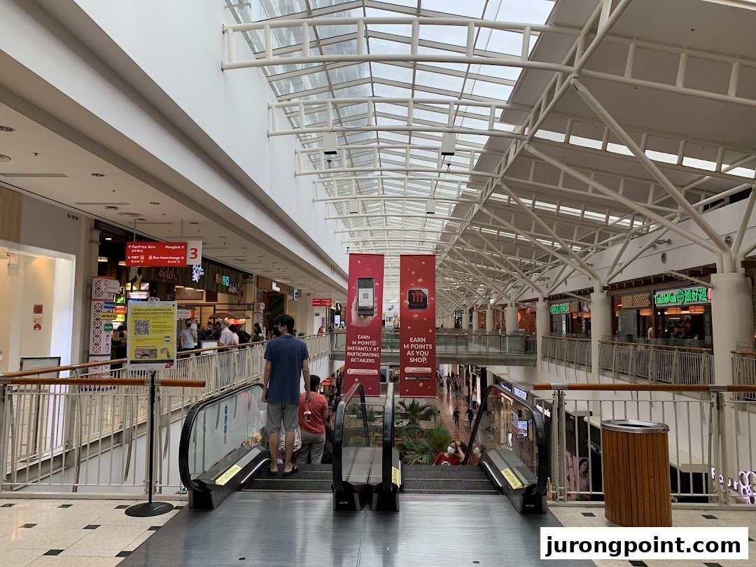 View of a bustling shopping mall interior with escalators and various retail outlets.