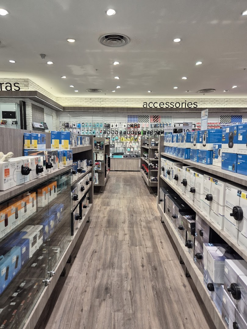 An aisle inside Harvey Norman showcasing cameras, accessories, and various electronics on display shelves.