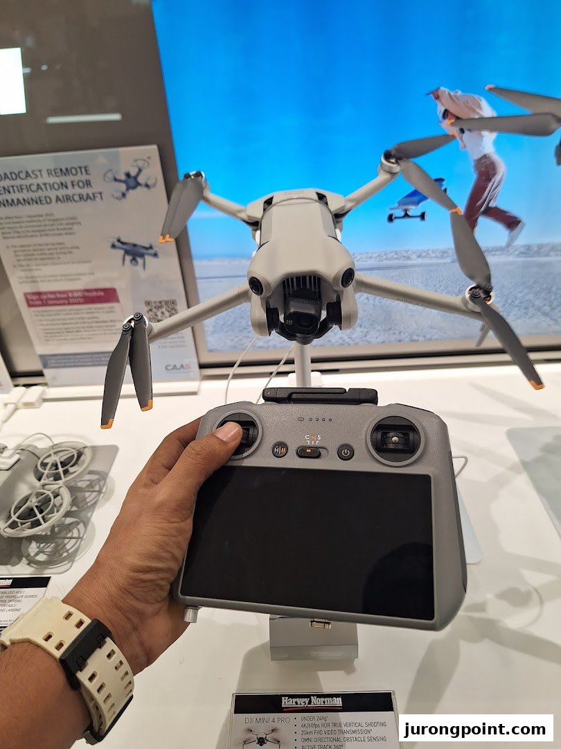 A customer's hand holds a DJI drone controller, with a DJI Mini 4 Pro drone on display at Harvey Norman.