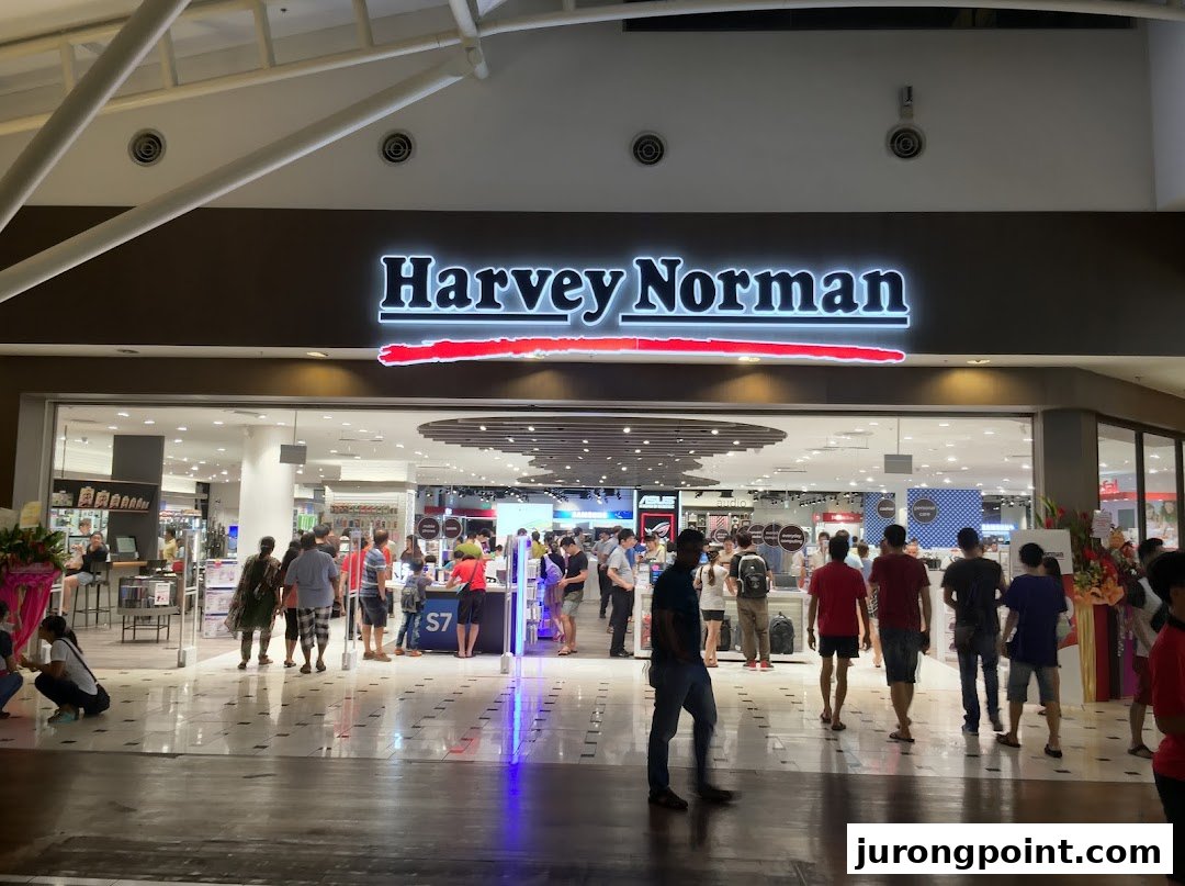 The brightly lit entrance of Harvey Norman at Jurong Point, bustling with shoppers exploring electronics and home goods.