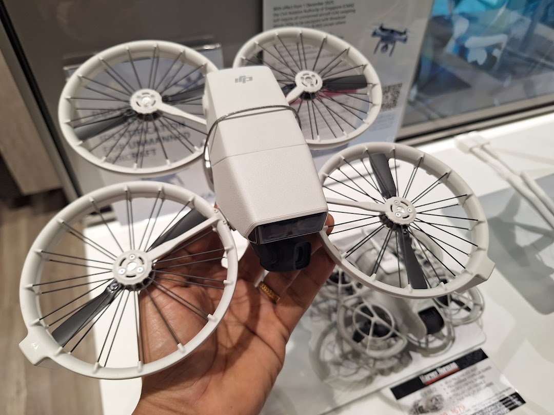 A hand holds a white DJI drone with propeller guards, showcasing electronics available at Harvey Norman.