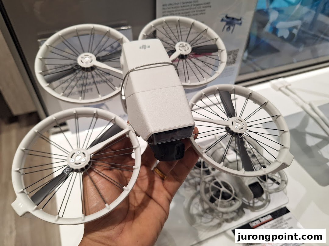 A hand holds a white DJI drone with propeller guards, showcasing electronics available at Harvey Norman.