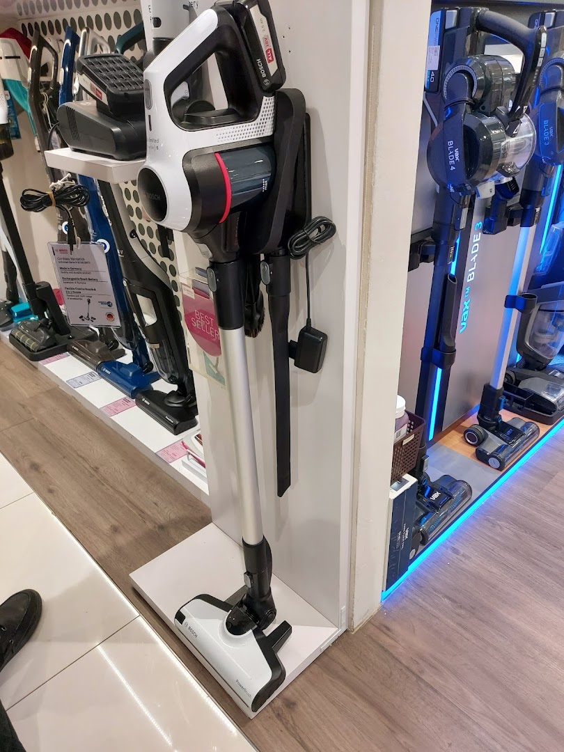 A display of modern cordless vacuum cleaners, including Bosch and Vax models, inside a retail store.