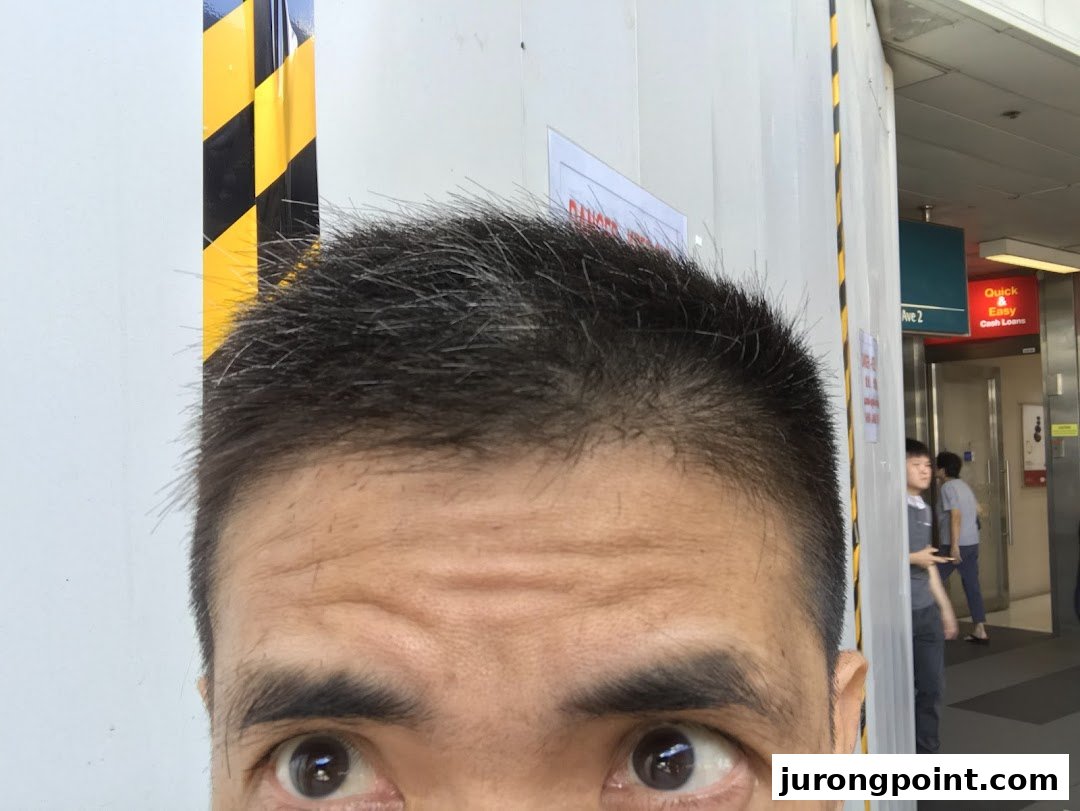A close-up of a person's head, focusing on their eyes and short hair, with background elements.