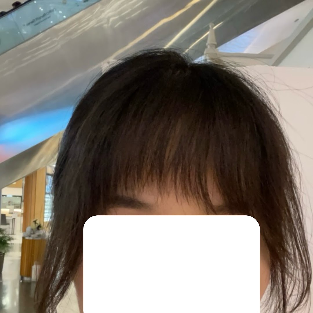 A close-up of a person's head with dark hair and bangs, taken inside a modern interior.