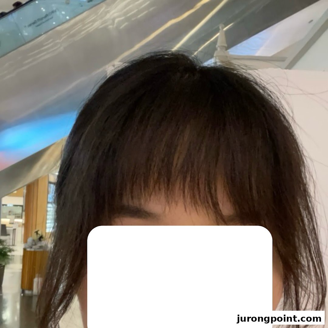A close-up of a person's head with dark hair and bangs, taken inside a modern interior.