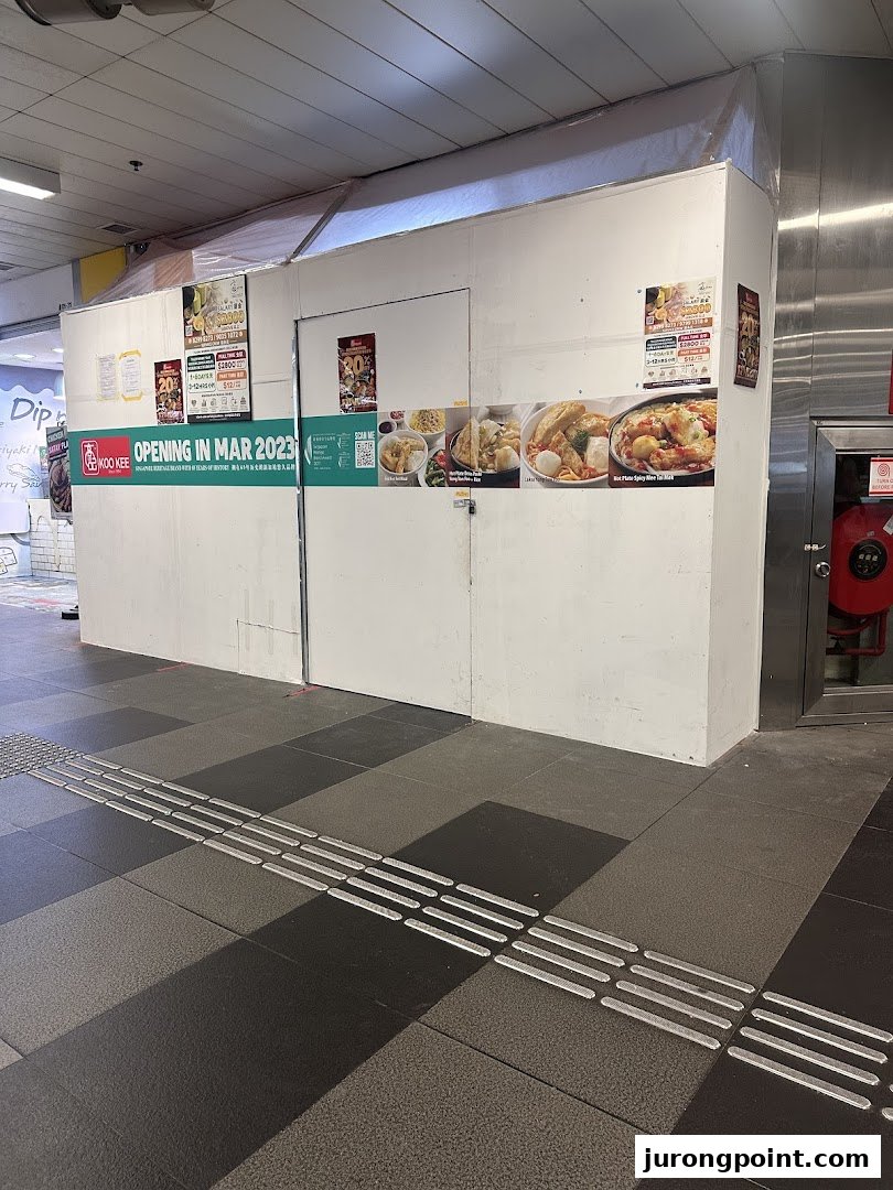 A boarded-up shop front for 'KOO KEE' announcing its opening in March 2023, featuring enticing food images.