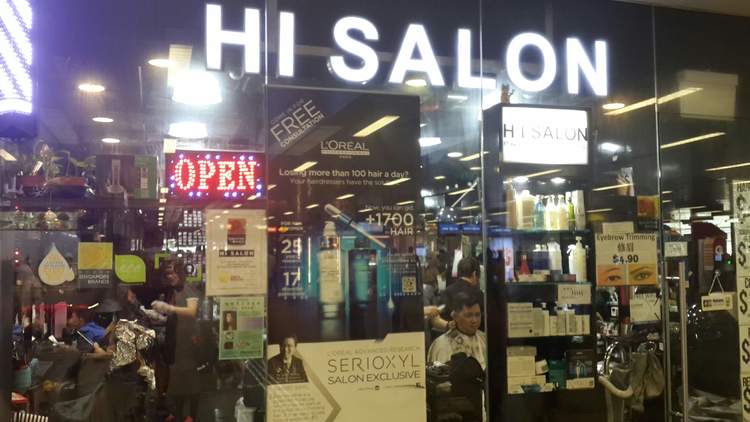 The brightly lit storefront of HI Salon, featuring an 'OPEN' sign and promotional displays for hair and beauty services.